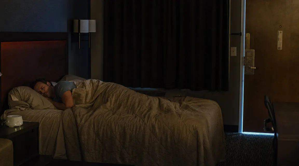 Trucker sleeping soundly in a motel room with a white noise machine on the nightstand