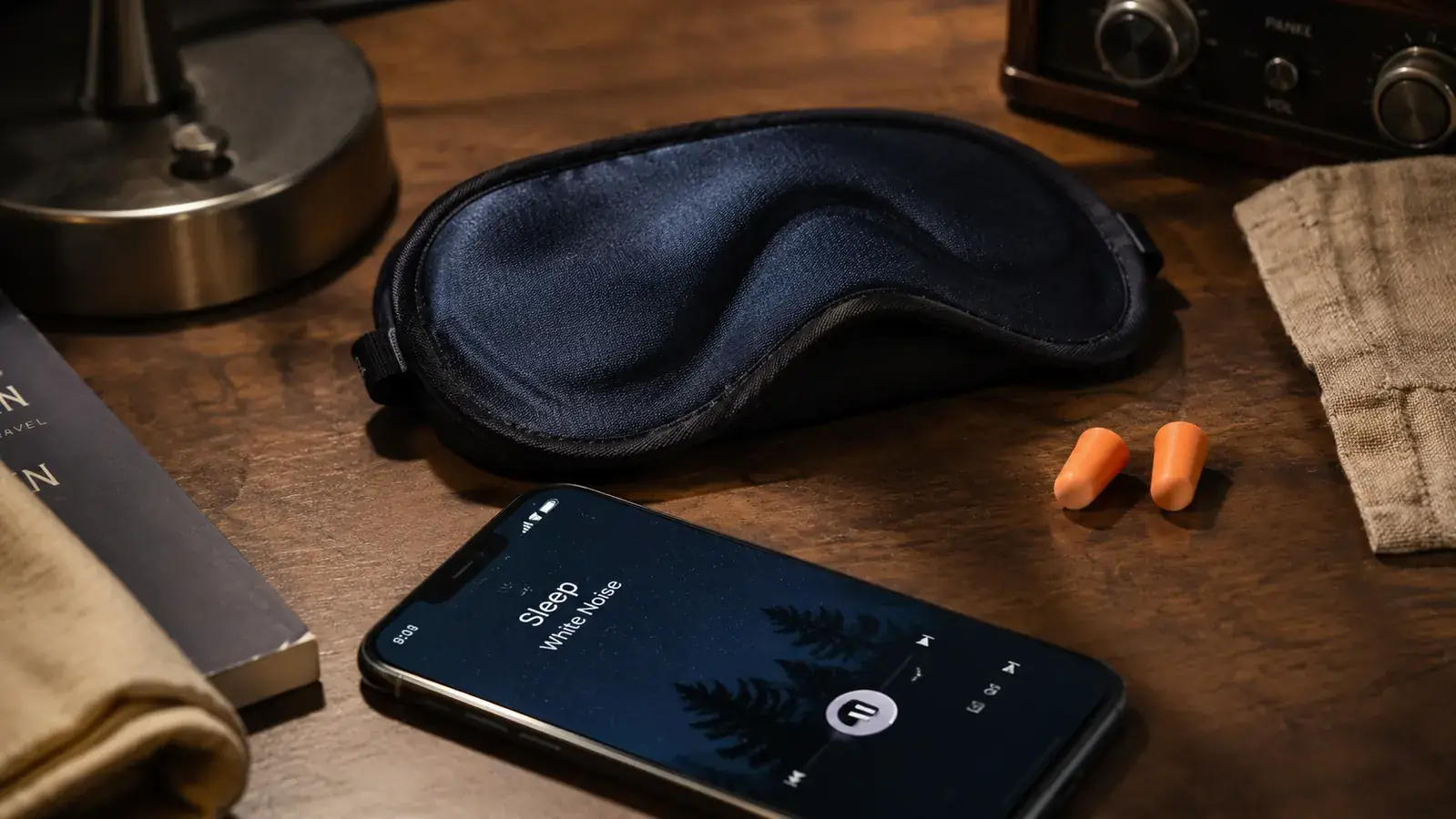 Sleep mask, foam earplugs, and white noise app on a phone laid out on a truck dash as a sleep kit