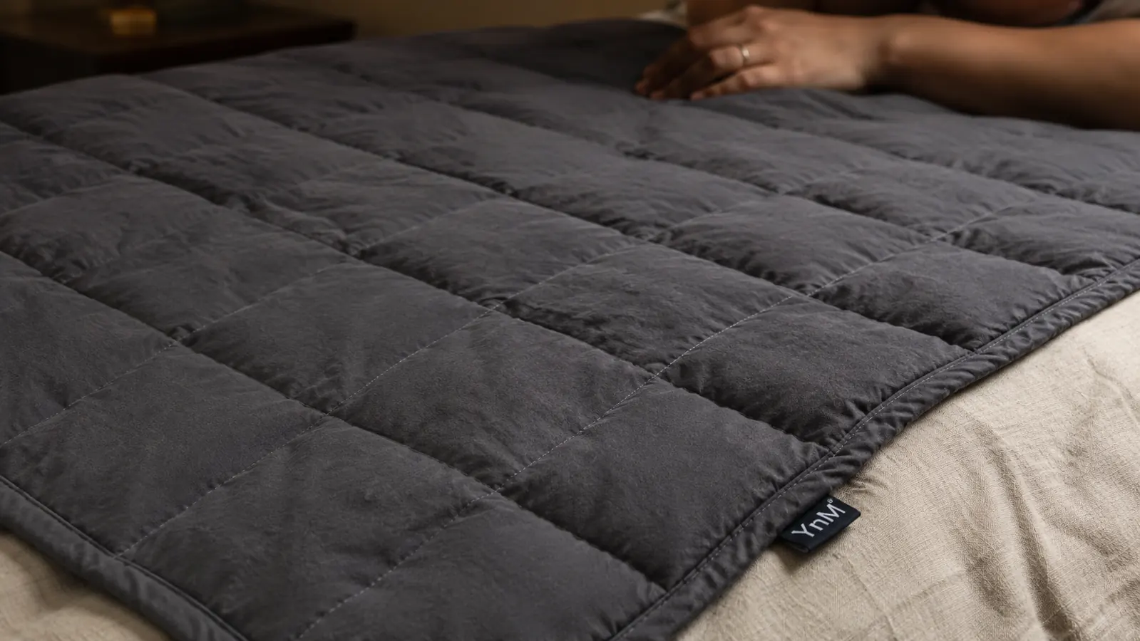 YnM weighted blanket spread across a bed showing the small square grid stitching pattern that holds the glass beads in place